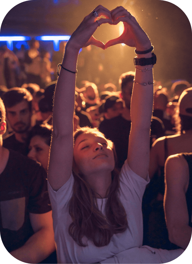 Young woman in front of a crowd raising her arms making a heart shape with her hands